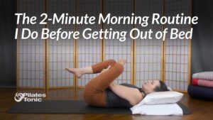 Sydney lying on a mat with her head on pillows, hugging one knee to her chest while extending the other leg in a gentle morning stretch.
